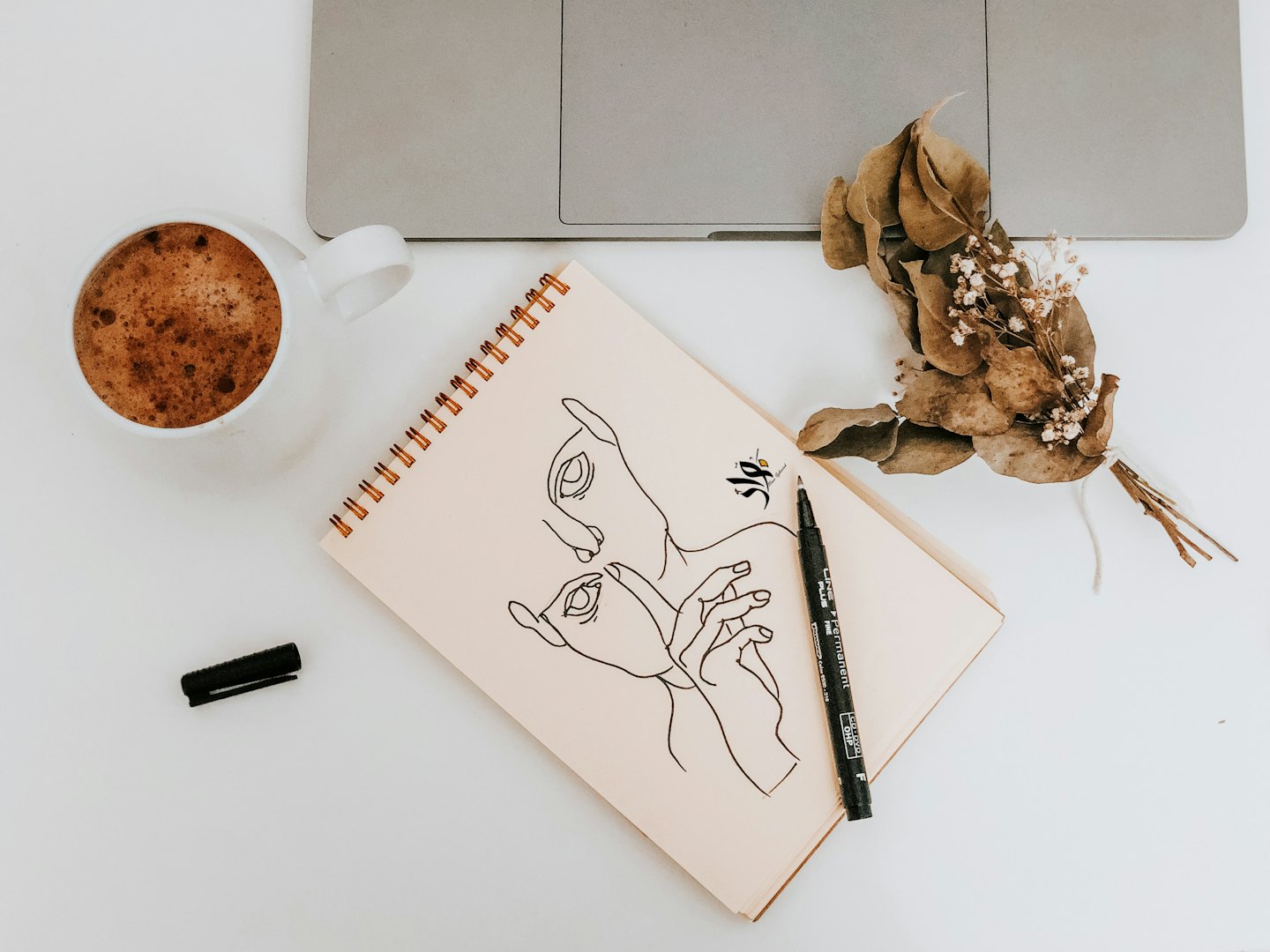 Koffie, laptop en notitieboek met schetsen op een bureau.