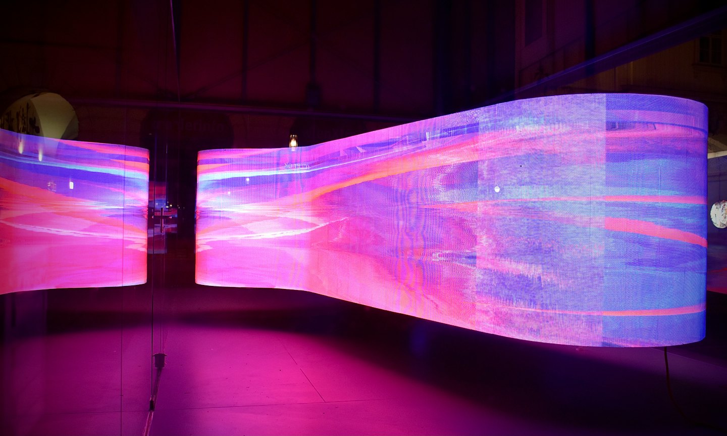 Gebogen LED-schermen tonen levendige abstracte kunst in een donkere kamer.
